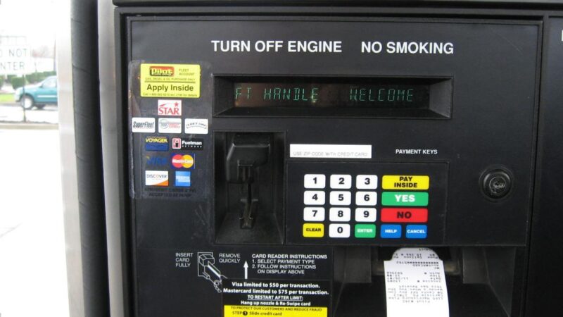 Pessoa abastecendo carro em posto de gasolina e usando cartão de crédito no aplicativo