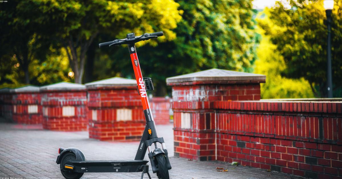 Scooter elétrica branca estacionada em rua urbana arborizada